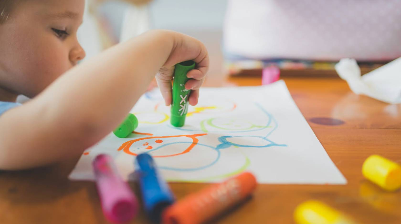 A child at a table draws on a piece of paper with crayons