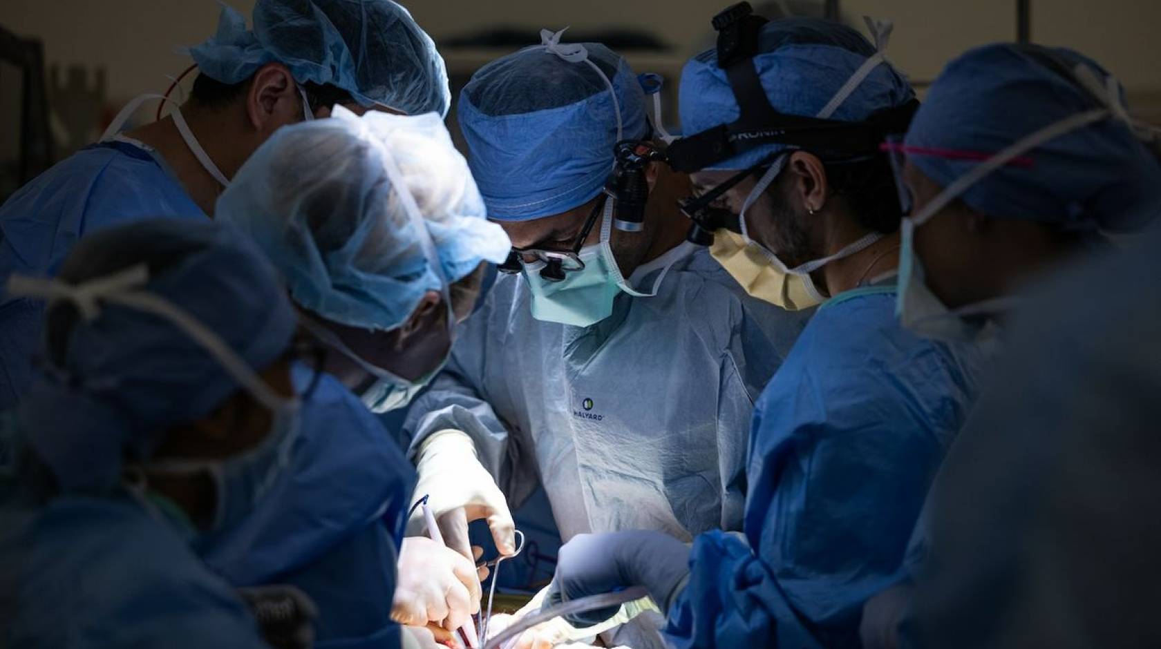 Six surgeons huddle around someone while operating