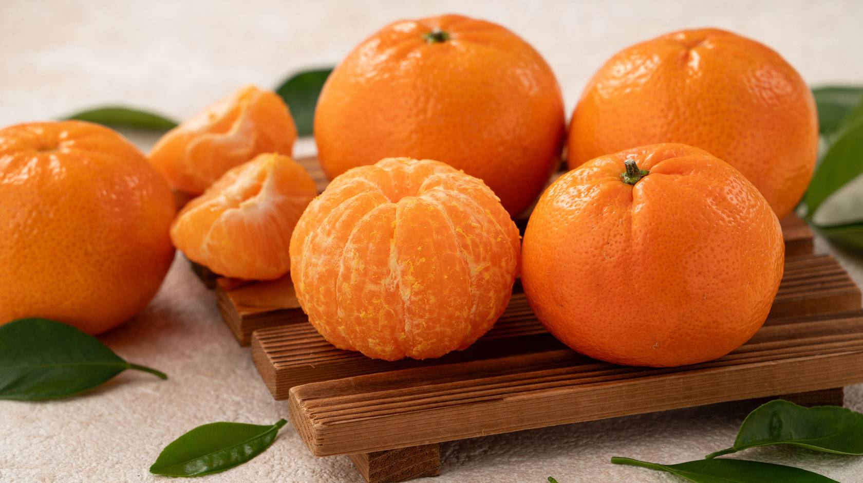 Five mandarin oranges on a cutting board with leaves arranged in a still-life imagte