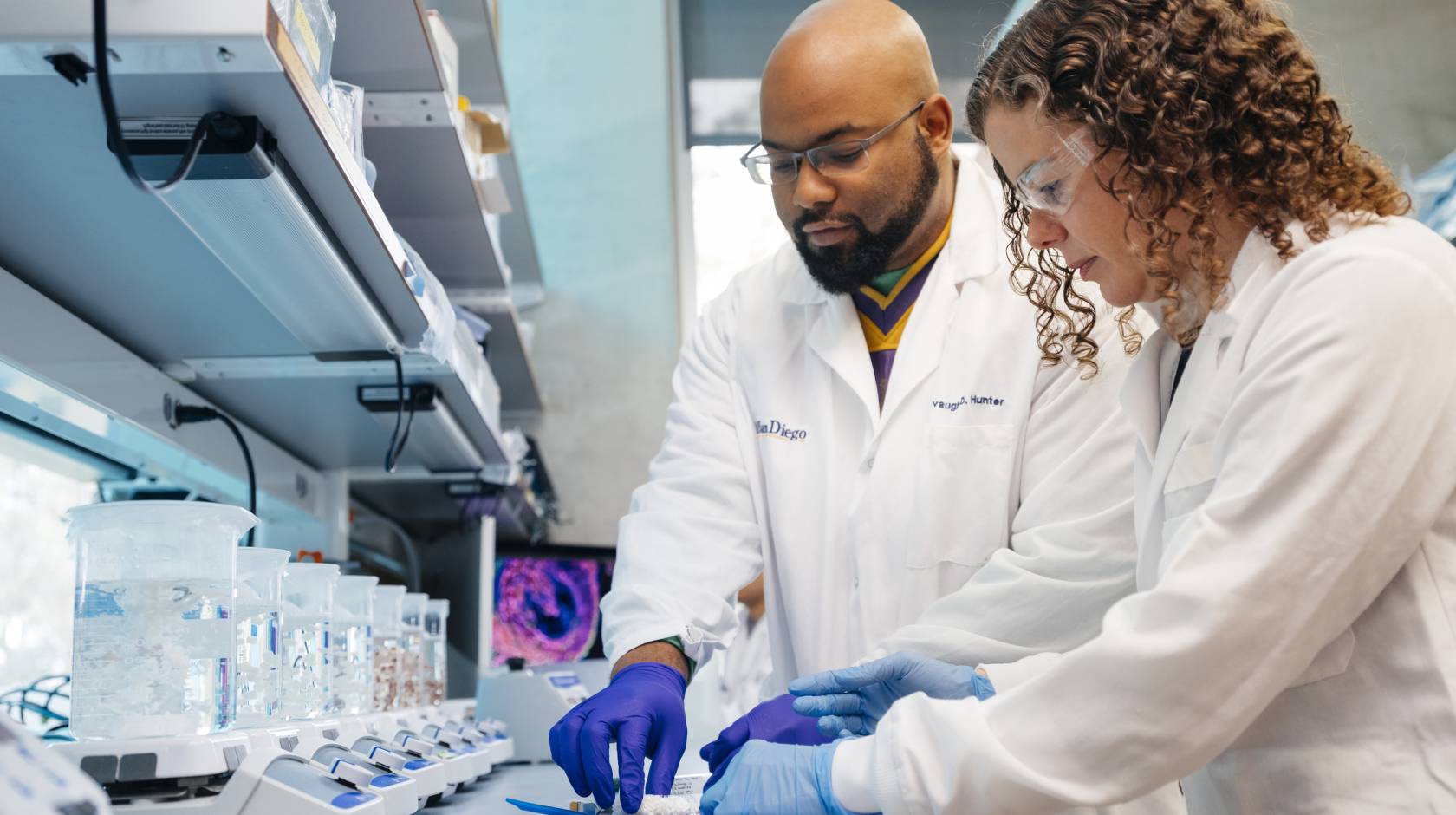 Two people in lab coats work in a lab together
