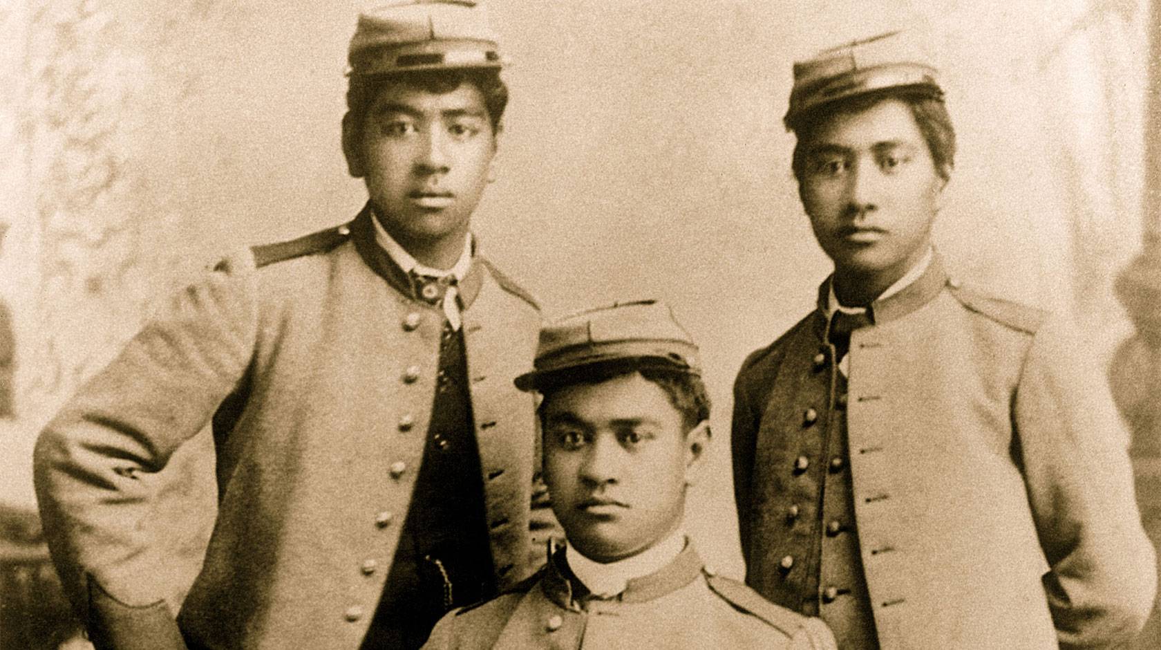 A sepia-toned historical portrait of three young Hawaiian men wearing military uniform
