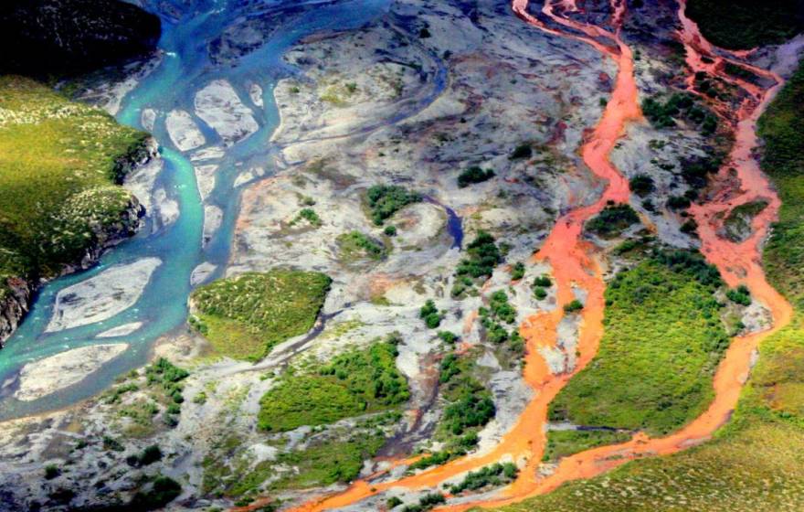 Aerial view of a braided river flowing through a tundra. The channels on the right side of the image are bright orange.