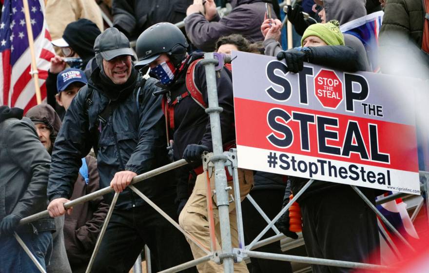 People wearing tactical gear attack the Capitol on Jan 6th, with a big sign reading "Stop the Steal"