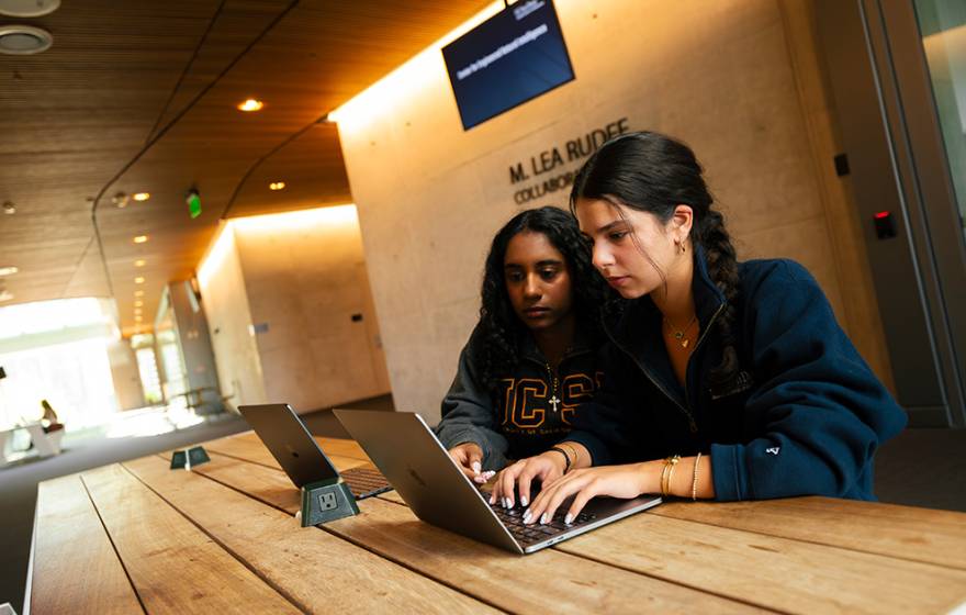Two young women sit together looking at a computer