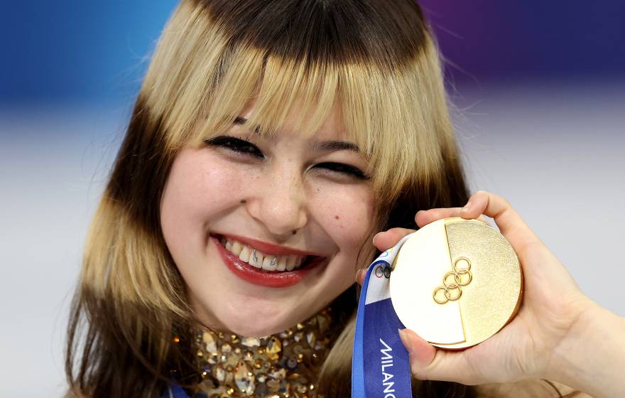 A woman holds up a gold medal and smiles