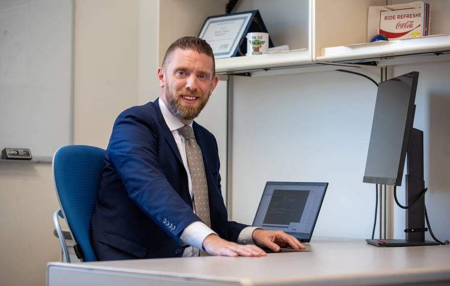 Andy Crosby at his desk, smiling at the camera, wearing a blue suit