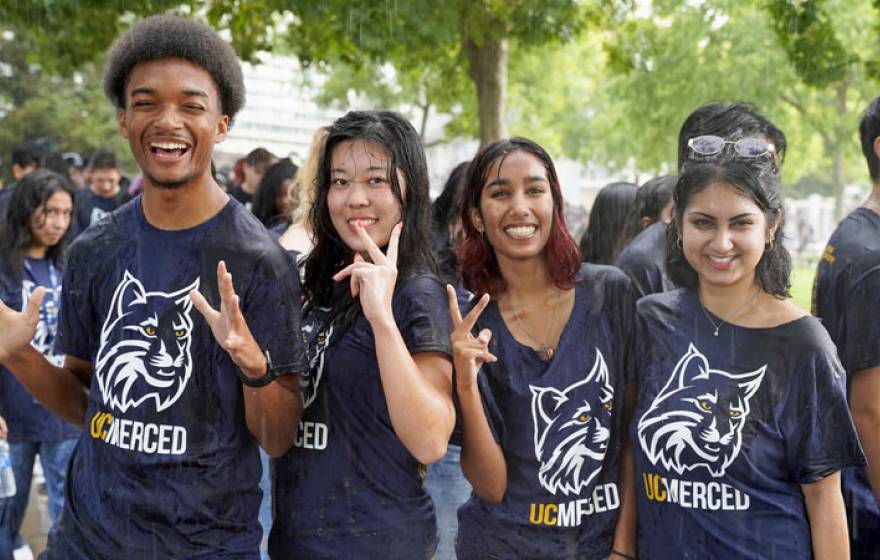 Five students wearing UC Merced Bobcat t-shirts smile for the camera in a downpour
