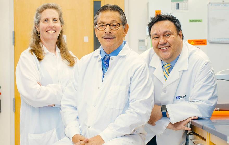 Three doctors with white lab coats pose together in a lab and smile