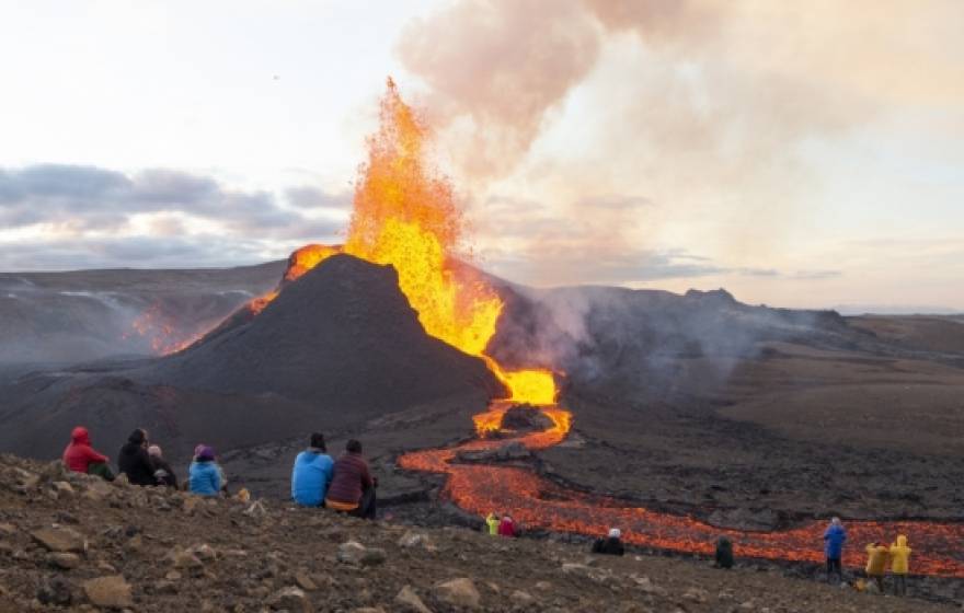 People sitting on a hillside watching Iceland’s Fagradalsfjall erupt
