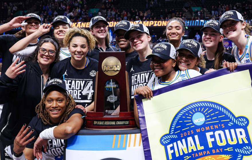 The UCLA women's basketball team in Final Four gear smiles for a group picture around the Spokane regional trophy