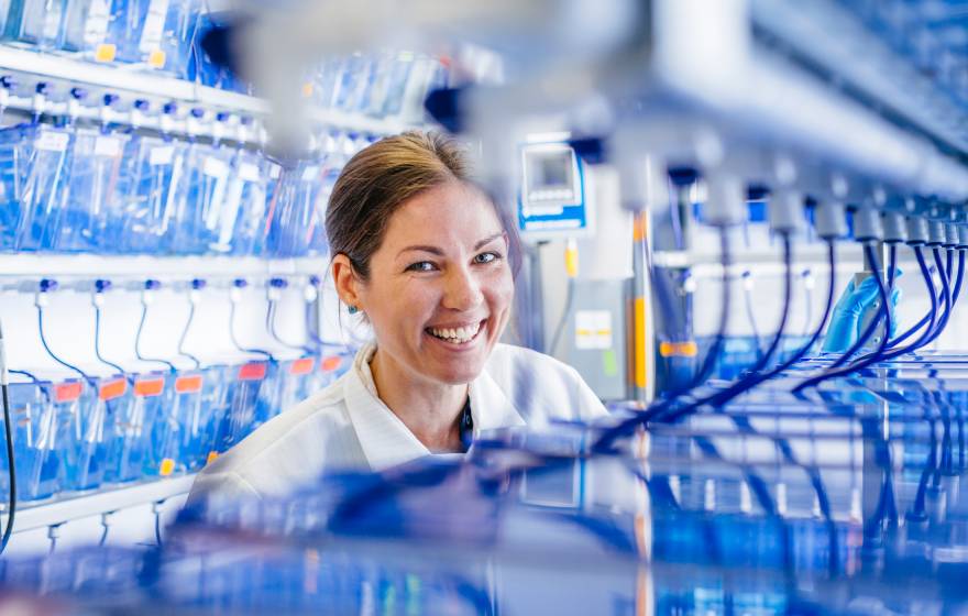 A student researcher smiles in a lab coat around blue tubing