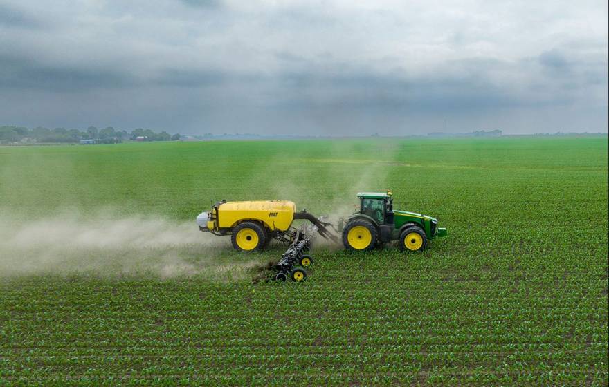 A tractor sprays pesticides on a green field under a gray sky