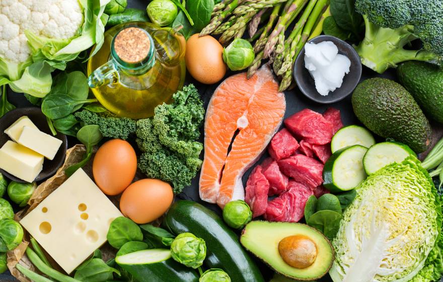 Assortment of healthy ketogenic low carb food ingredients for cooking on a kitchen table. Green vegetables, meat, salmon, cheese, eggs.