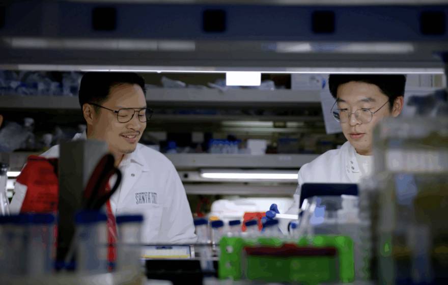 Two scientists in white coats work at a lab bench