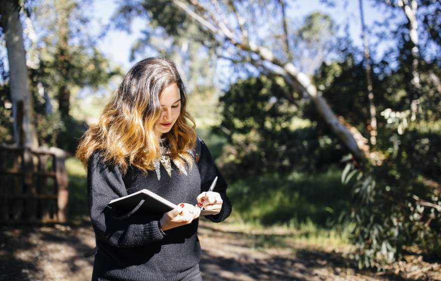 Young woman writing in notebook walking through woods