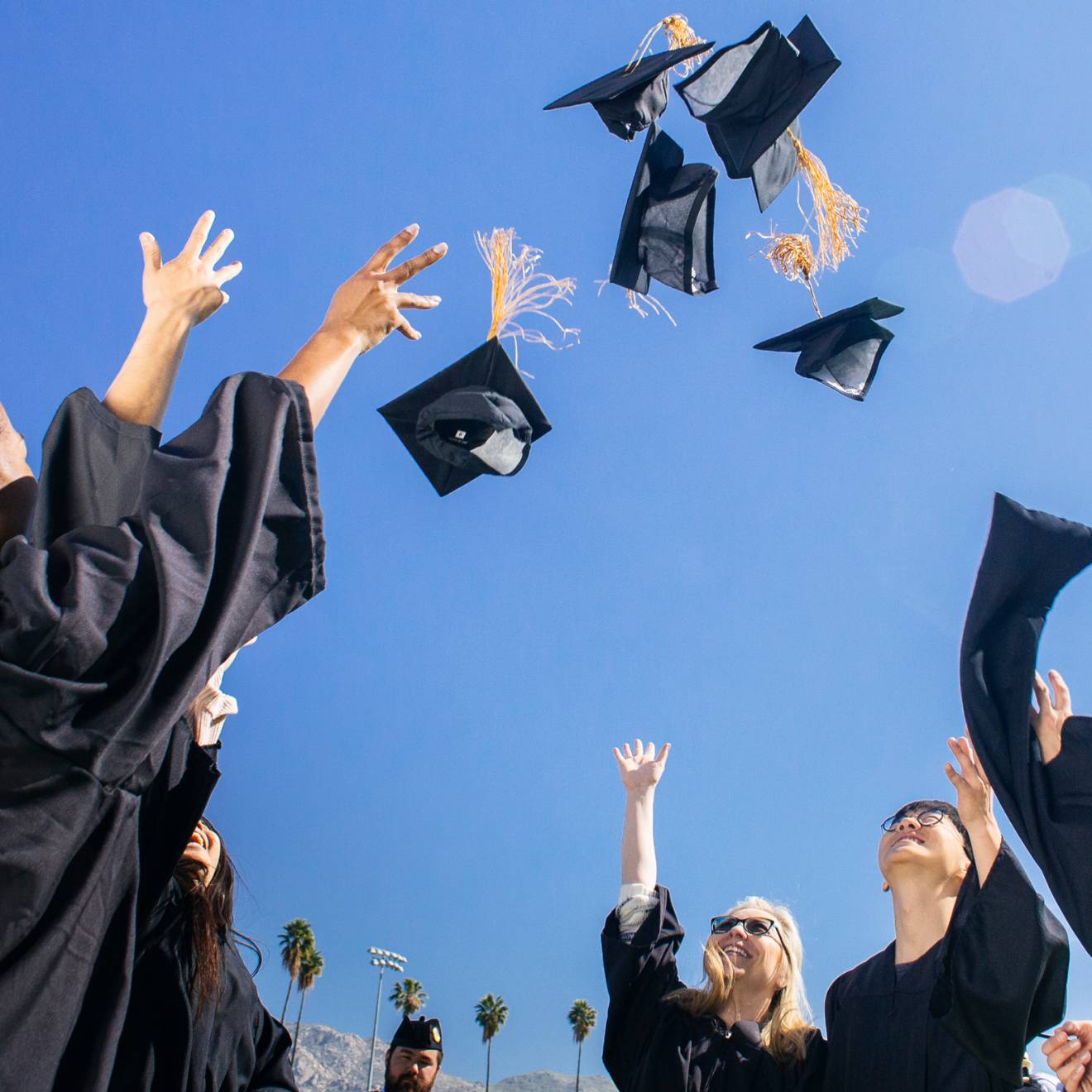 College graduates in black robes throwing their caps in the air against a blue sky
