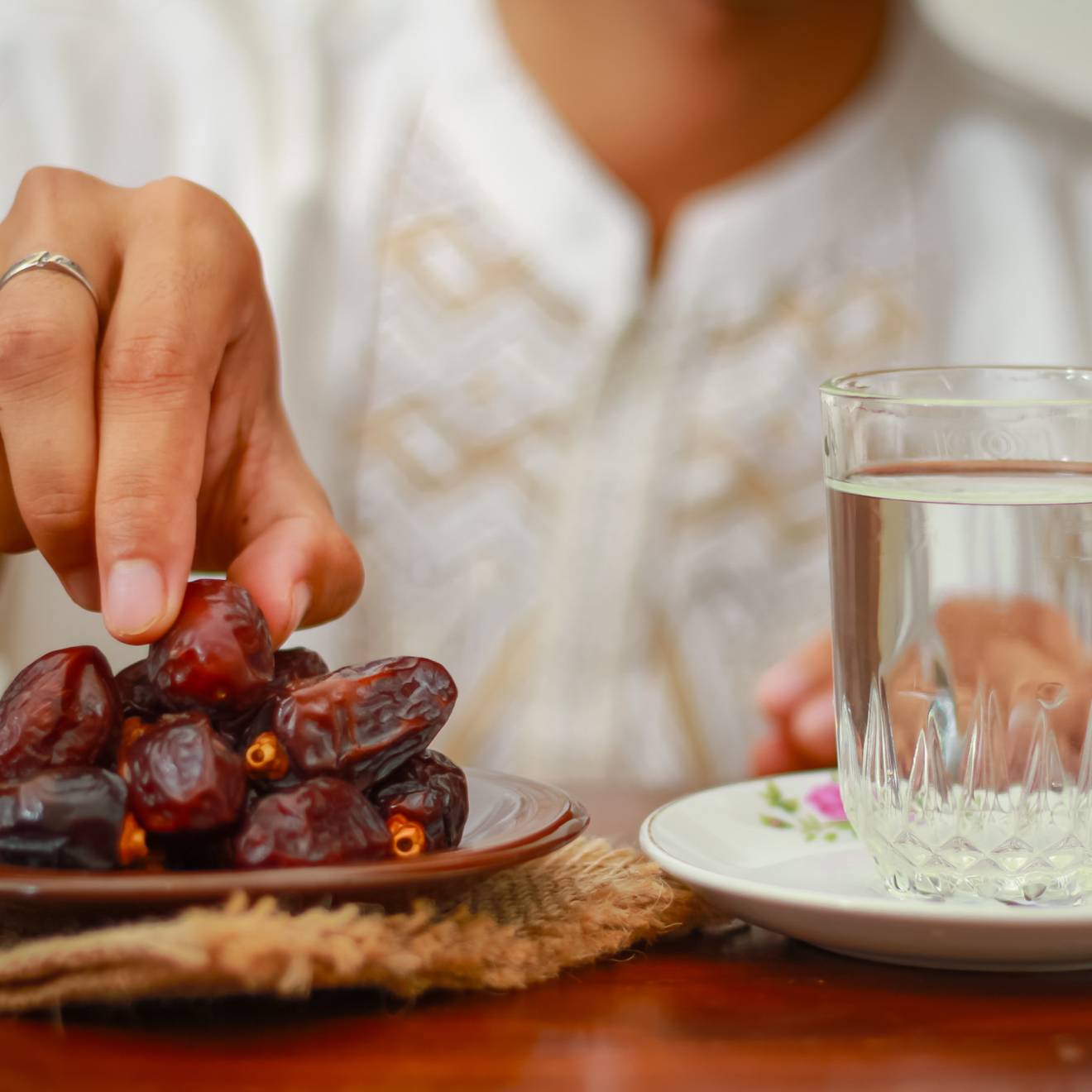 A plate full of dates and a glass of water, with a hand reaching for a date