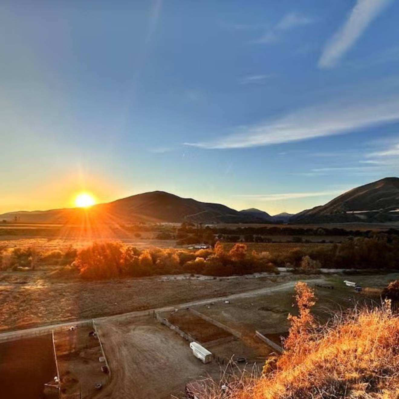 Sunrise over rolling hills, casting warm light on the landscape and clear blue sky.