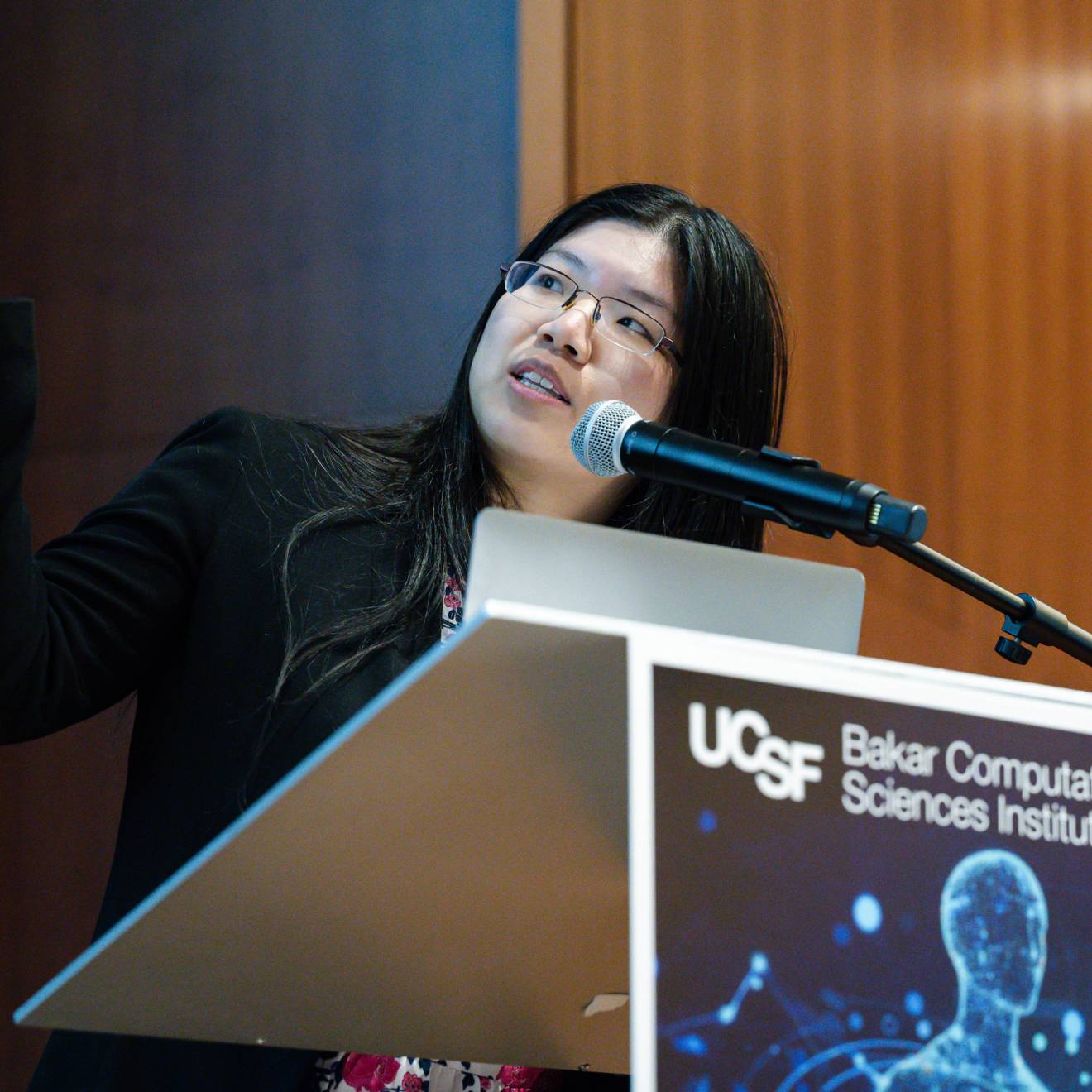 A young woman points at a screen off-camera while at a UCSF lectern
