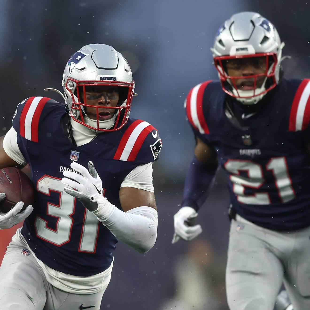 Two players for the New England Patriots, one holding the football and running