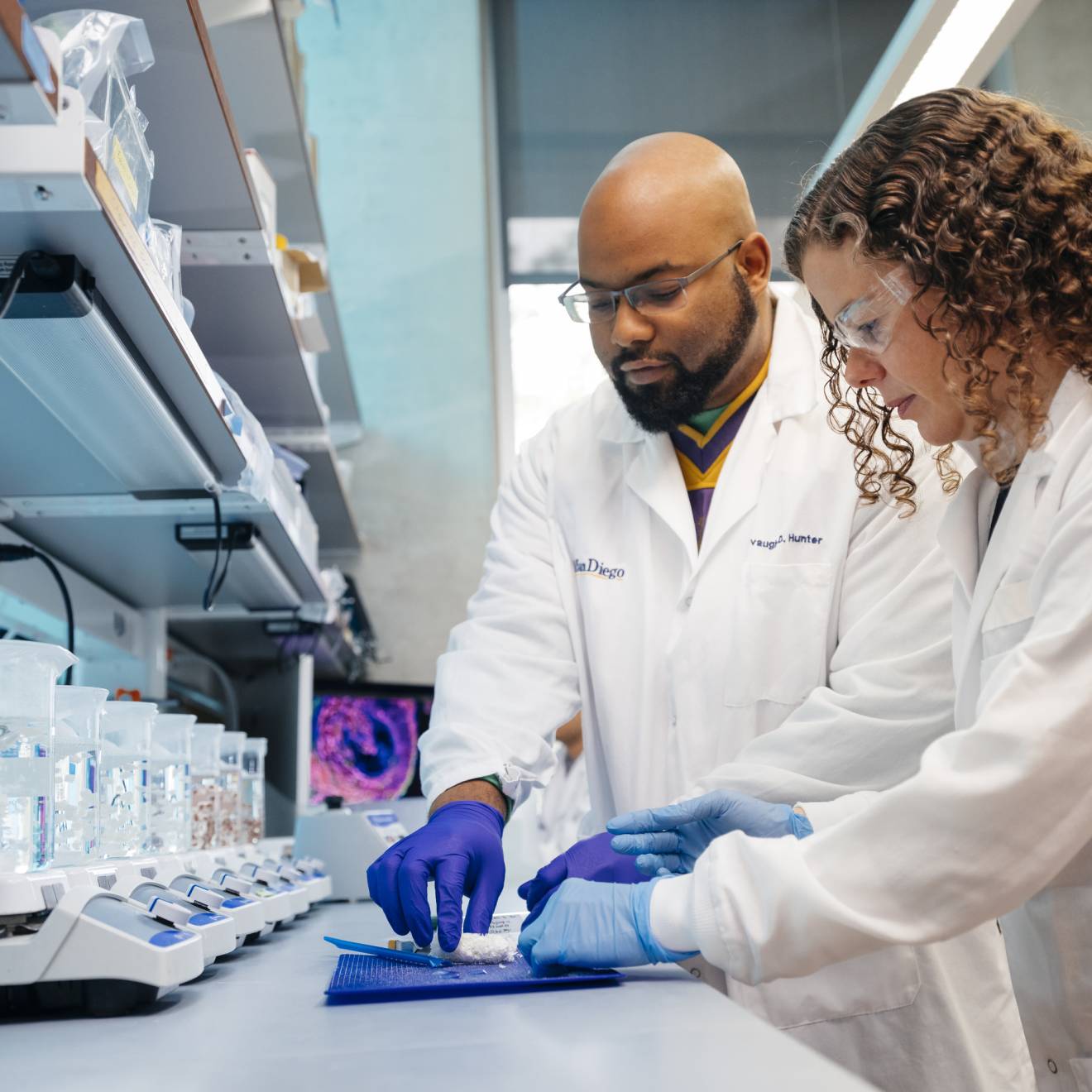 Two people in lab coats work in a lab together